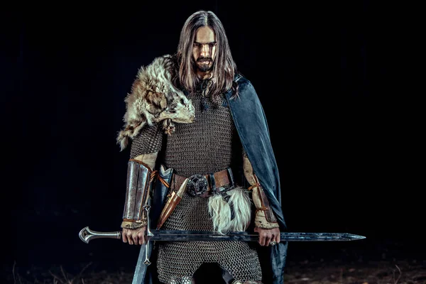 Uzun saçlı knight iki elle kılıç ile. Kayaların üzerinde arka plan.