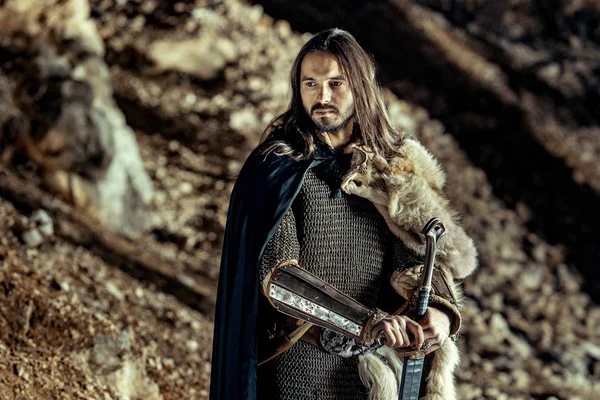 长头发的骑士用双手剑 背景上的岩石 — 图库照片
