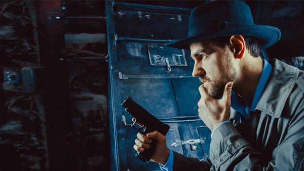 Detective with the gun wearing a fedora hat and a trench coat, dark background. — Stock Photo, Image