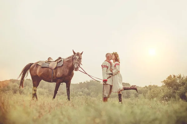 Dojrzały mężczyzna i kobieta w etniczne ubrania są Całowanie w pobliżu koń na tle obszarów wiejskich. — Zdjęcie stockowe