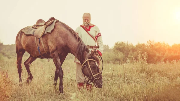 L'uomo in abiti etnici pascola un cavallo sullo sfondo dei campi estivi . — Foto Stock