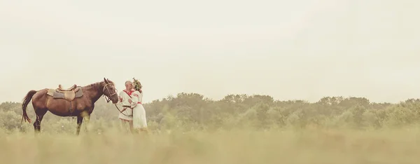 Зрелый мужчина и женщина в этнической одежде целуются возле лошади на — стоковое фото