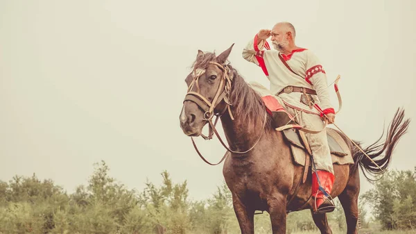 Man in ethnic clothing with the bow is riding a horse and searching for enemy. — Stock Photo, Image