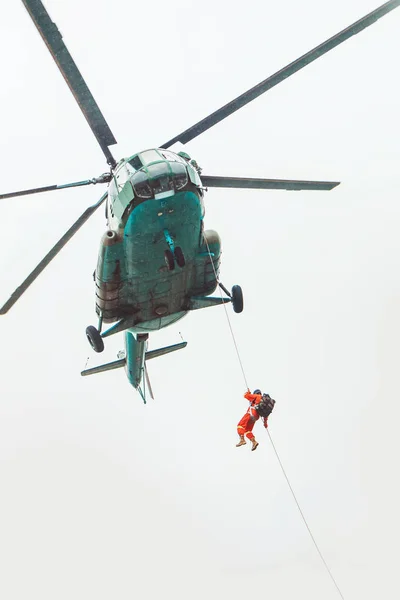 Hélicoptère de sauvetage et sauveteur sur la corde - véhicule volant de sauvetage sur fond de ciel pluvieux . — Photo