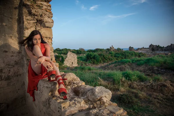 Mujer vestida de rojo está sentada en las ruinas de una antigua ciudad, Side, Turquía —  Fotos de Stock