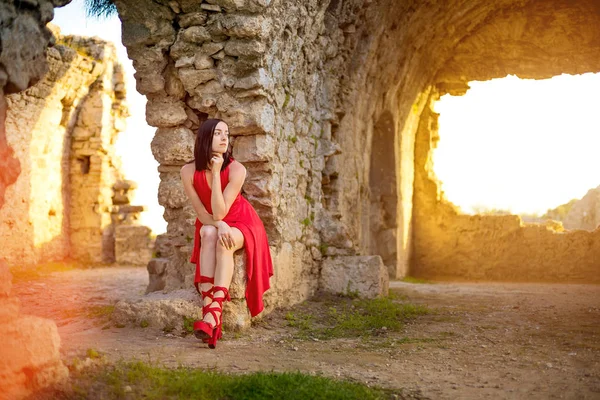 Kırmızı elbiseli kadın antik bir şehrin kalıntılarında oturuyor, Side, Antalya, Türkiye — Stok fotoğraf