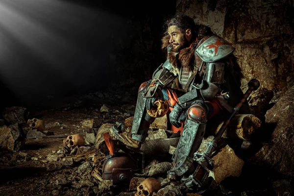 Potężny rycerz w zbroi z młotkiem siedzi na kamieniu. Dungeon na tle. — Zdjęcie stockowe