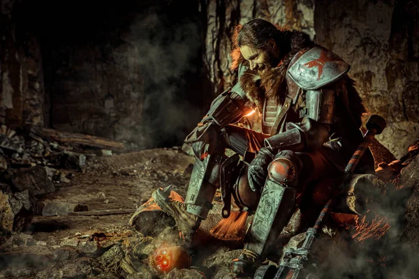 Potężny rycerz w zbroi z młotkiem siedzi na kamieniu. Dungeon na tle. — Zdjęcie stockowe