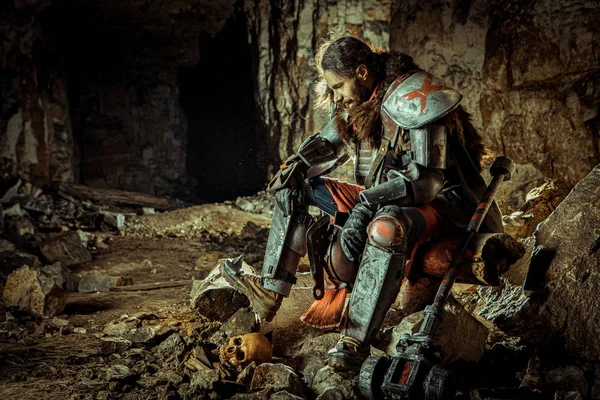 Der mächtige Ritter in der Rüstung mit dem Hammer sitzt auf dem Stein. Verlies im Hintergrund. — Stockfoto