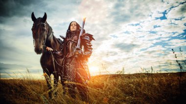 Ortaçağ şövalyesi zırhlı bir kız günbatımı tarlalarına karşı bir atla
