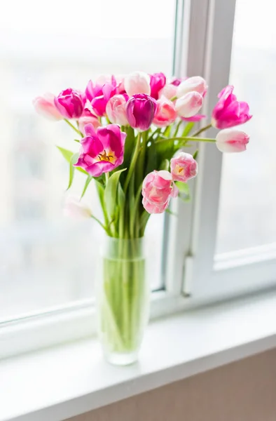 Bouquet of pink tulips in glass vase on window sill. Soft selective focus.