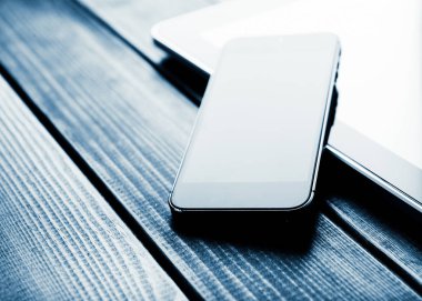 ahşap masa üzerinde telefon ve tablet pc. Tonda mavi 