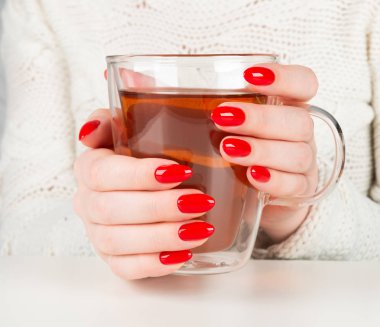 şeffaf bir fincan sıcak çay tutan eller. Güzel kırmızı manikür