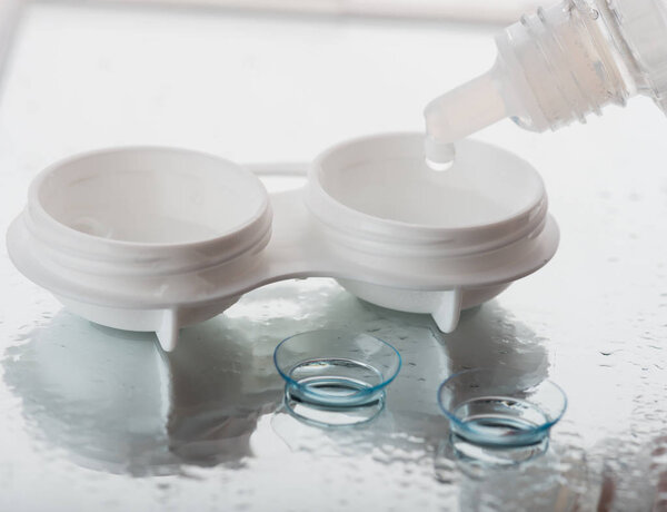Bottle with contact lenses solution and case on table, closeup view