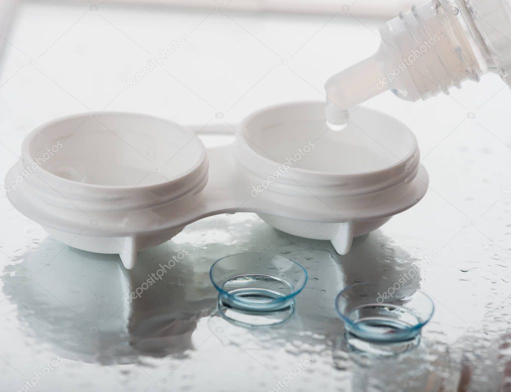 Bottle with contact lenses solution and case on table, closeup view