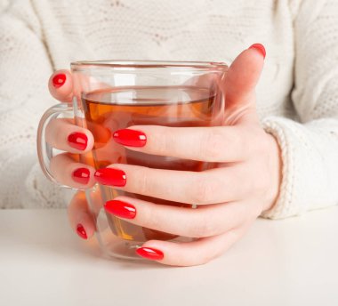 şeffaf bir fincan sıcak çay tutan eller. Güzel kırmızı manikür