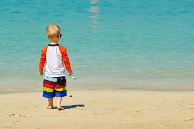 İki yaşındaki yürümeye başlayan çocuk kumsalda yürürken güneş gözlüğü 