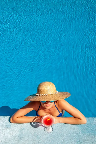 戴帽子的女人在游泳池边喝着国际化的鸡尾酒放松一下 — 图库照片