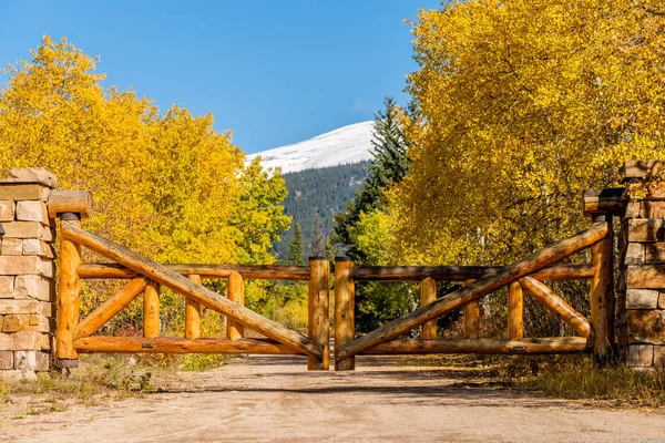 Rustic gate made of logs on unpaved road at autumn sunny day in Colorado, USA.