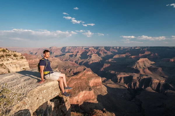 Tourist with backpack at Grand Canyon sitting on the rock edge, Arizona, USA