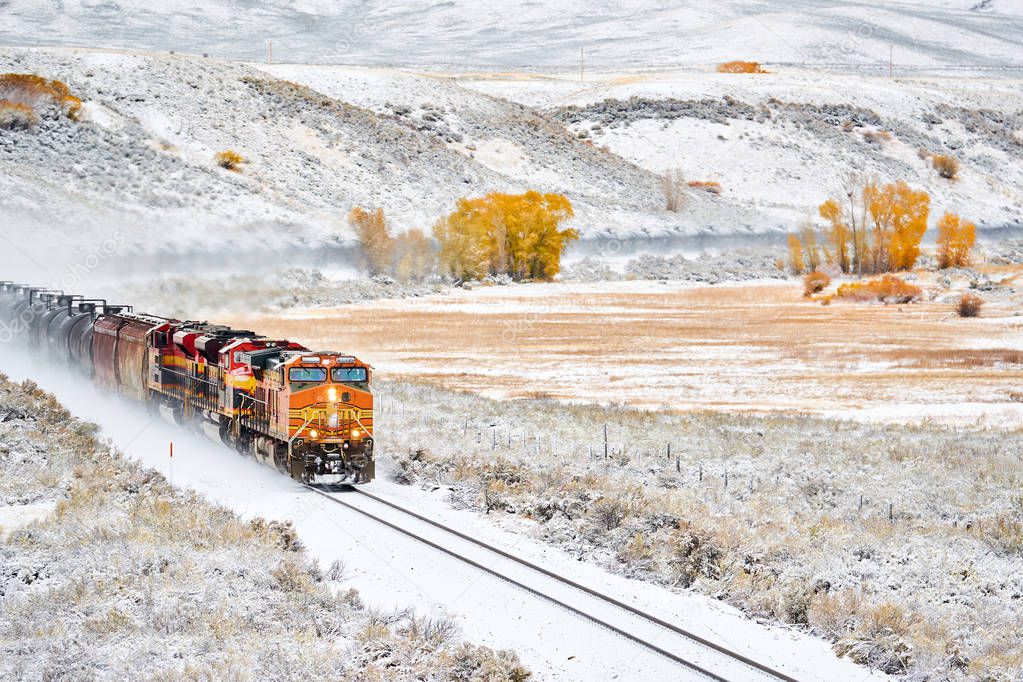 Train transporting tank cars. Season changing, first snow and autumn trees. Rocky Mountains, Colorado, USA. 