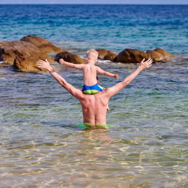 Plajda babasının omuzlarında iki yaşında bir yürümeye başlayan çocuk