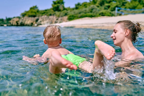 Two year old toddler boy learns to swim with mother