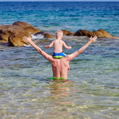 Plajda babasının omuzlarında iki yaşında bir yürümeye başlayan çocuk