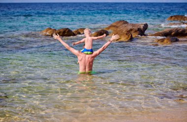 Plajda babasının omuzlarında yürümeye başlayan çocuk