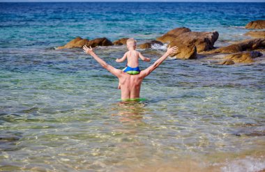 Plajda babasının omuzlarında yürümeye başlayan çocuk