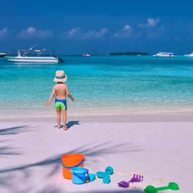 Üç yaşında bir çocuk sahilde oynuyor.