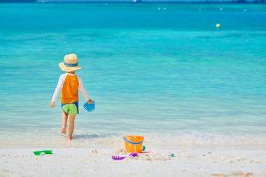 Üç yaşında bir çocuk sahilde oynuyor.