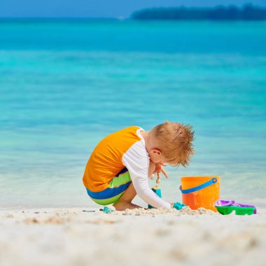 Üç yaşında bir çocuk sahilde oynuyor.