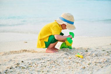 Üç yaşında bir çocuk sahilde oynuyor.
