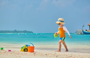 Üç yaşında bir çocuk sahilde oynuyor.