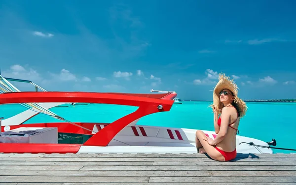 Mujer en bikini sentada en embarcadero con barco —  Fotos de Stock