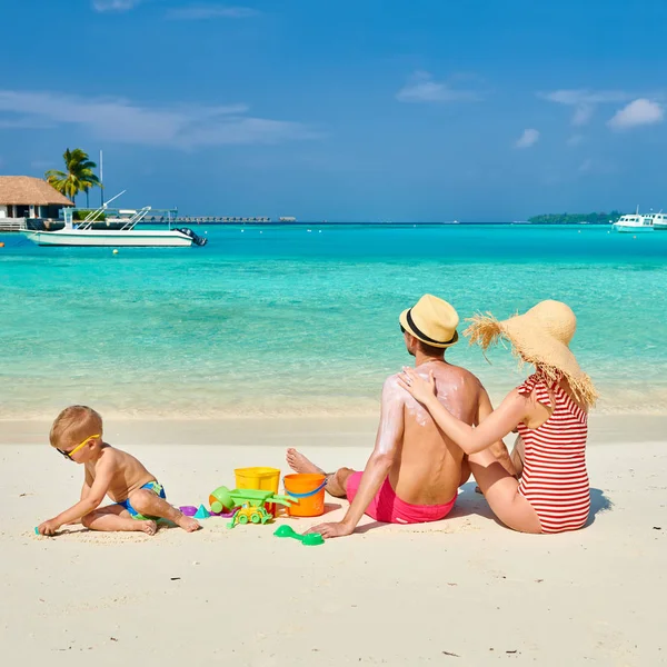 在海滩上的家人 和三岁男孩的年轻夫妇 女人在男人背上涂防晒霜 在马尔代夫的暑假 — 图库照片