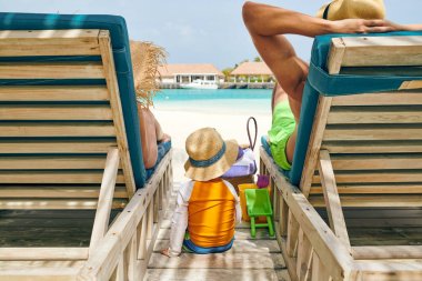 Ahşap yatak şezlong kumsalda, Aile, üç yaşındaki çocuk ile genç çift. Maldivler tatil yaz.