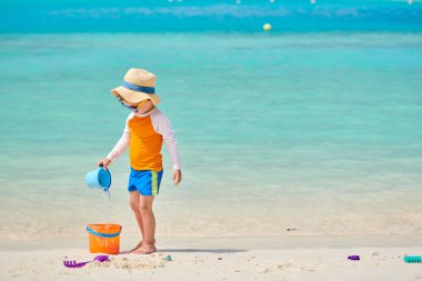 Üç yaşında bir çocuk sahilde oynuyor.