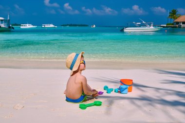 Üç yaşında bir çocuk sahilde oynuyor.