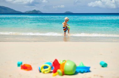 Üç yaşında bir çocuk sahilde plaj oyuncaklarıyla oynuyor. Seyşeller 'de yaz tatili, Mahe..