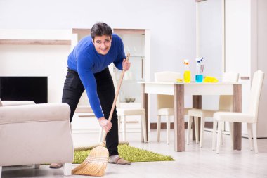 Genç adam yerleri süpürgeyle temizliyor.