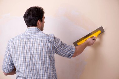 Evdeki duvara alçı yapıştıran genç adam.