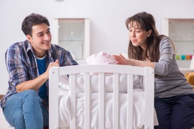 Yatağın yanında yeni doğmuş bebekleri olan genç ebeveynler.