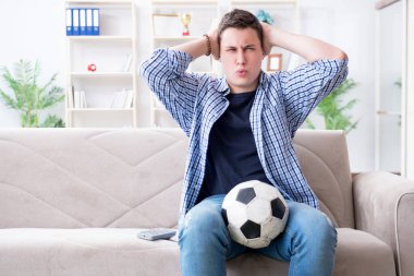Evde futbol izleyen genç bir öğrenci.