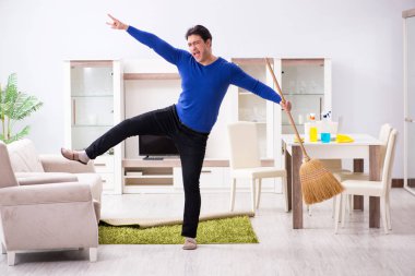 Genç adam yerleri süpürgeyle temizliyor.