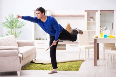 Genç adam yerleri süpürgeyle temizliyor.