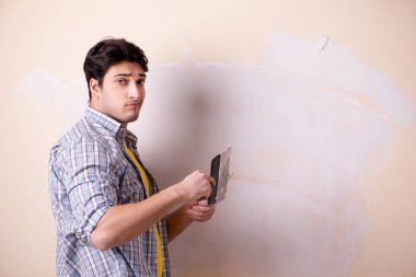 Young man applying plaster on wall at home clipart