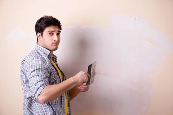 Ung man applicerar gips på vägg hemma — Stockfoto