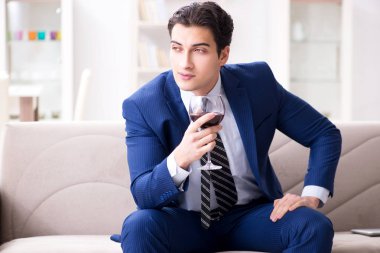 İş adamı evde oturmuş şarap içiyor.